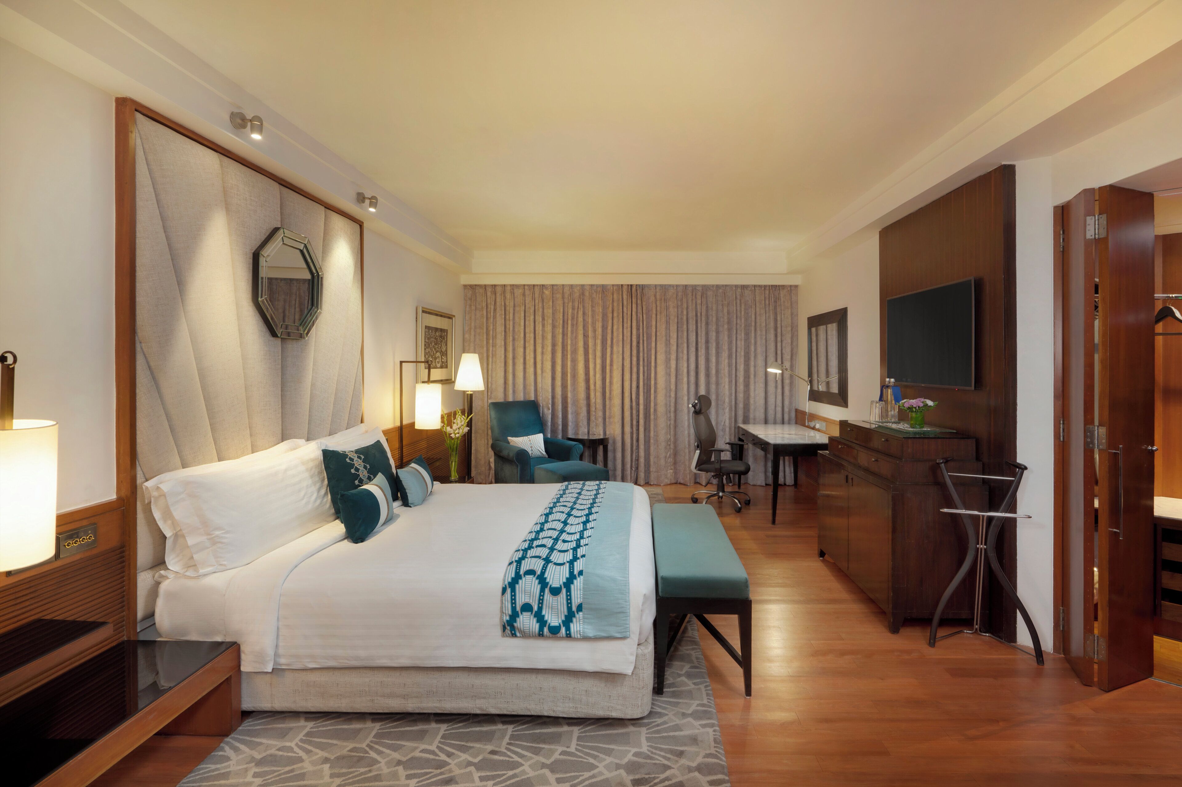 A hotel room with a large bed, a desk, a chair, a TV, and a wardrobe.