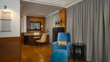 Uma sala de estar moderna com uma poltrona azul, piso de madeira, área de refeições com mesa e cadeiras, e uma cortina cinza grande.