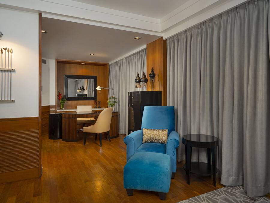Uma sala de estar moderna com uma poltrona azul, piso de madeira, área de refeições com mesa e cadeiras, e uma cortina cinza grande.
