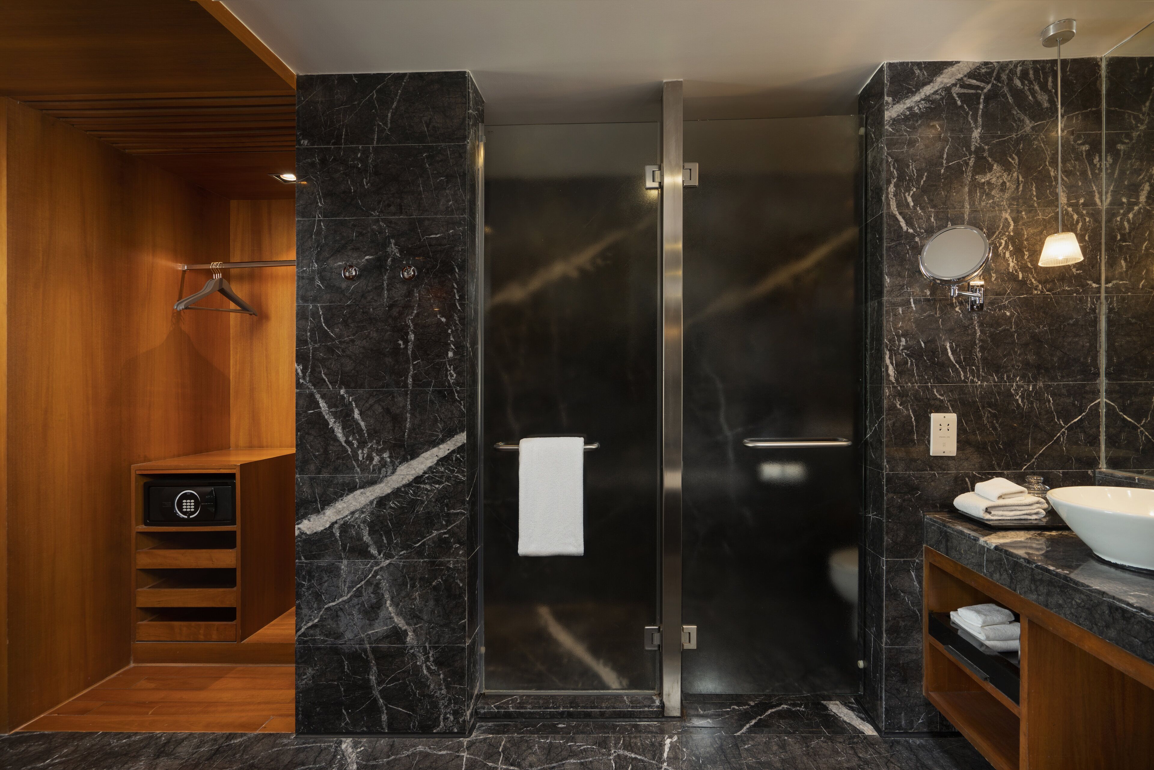 A modern bathroom with a glass shower enclosure, marble walls, a wooden vanity, and a towel rack.