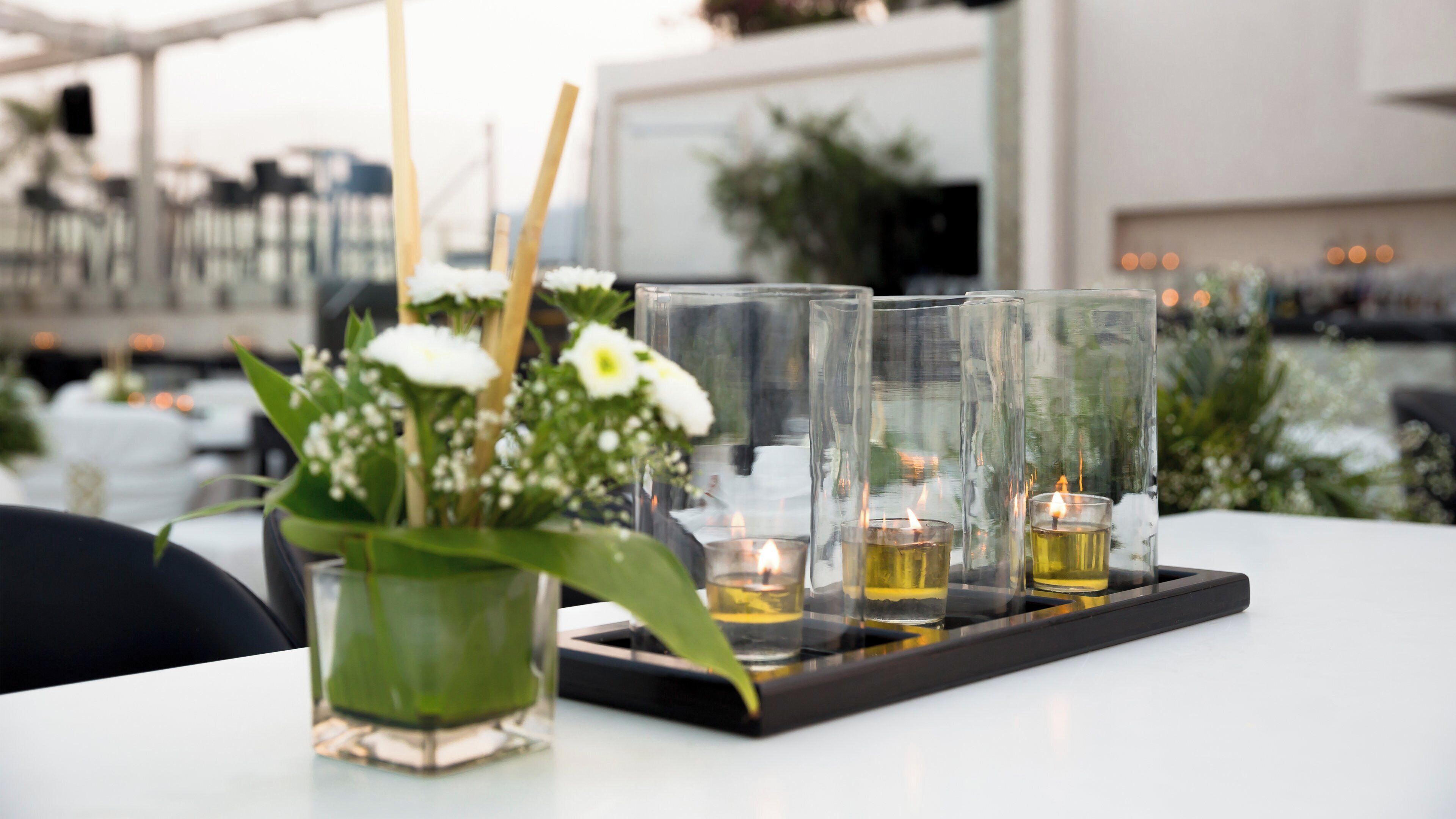 A table with a tray holding glasses and candles, surrounded by greenery and flowers.