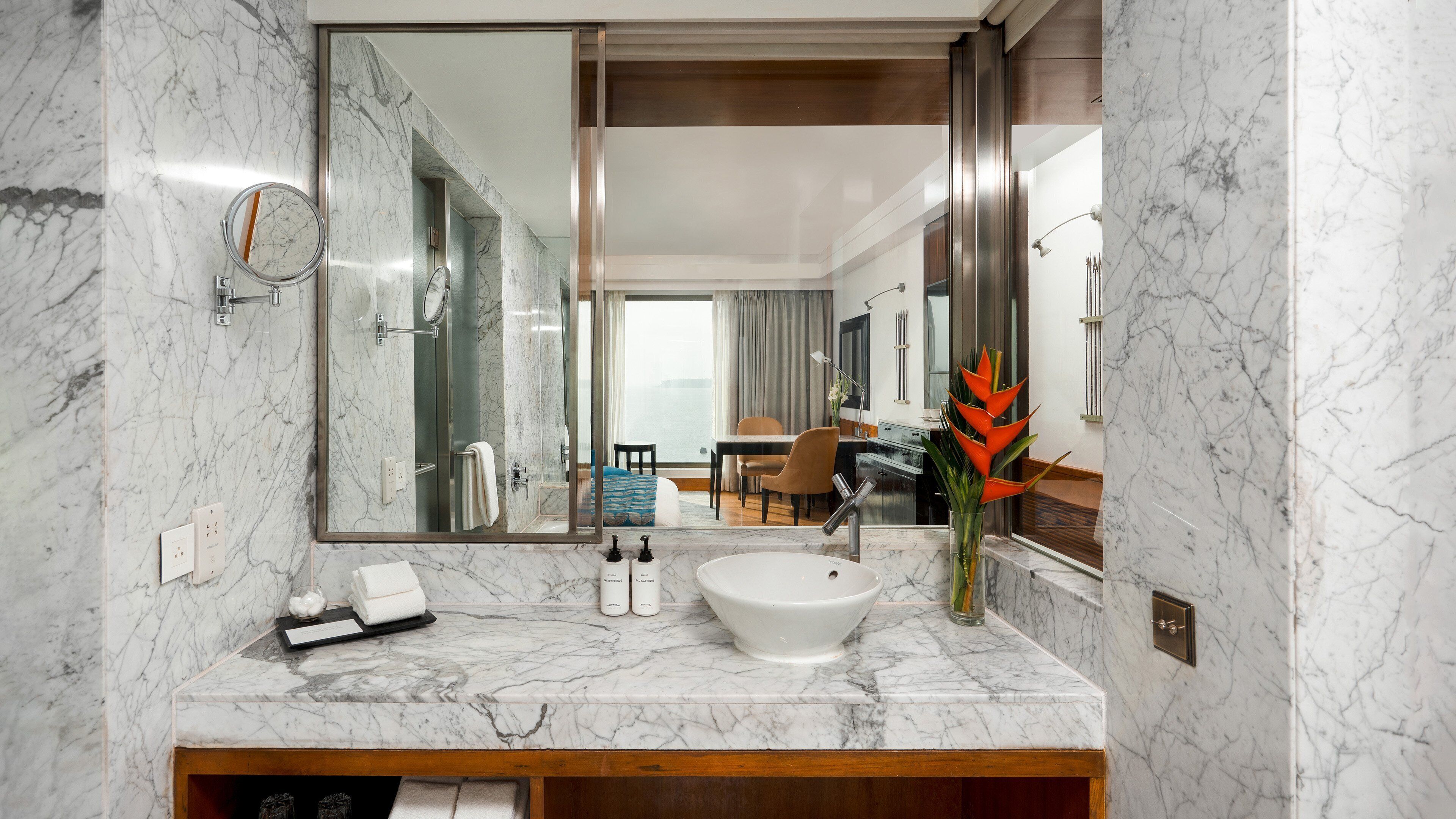 Un baño moderno con lavamanos de mármol, un espejo grande y vistas a un comedor.