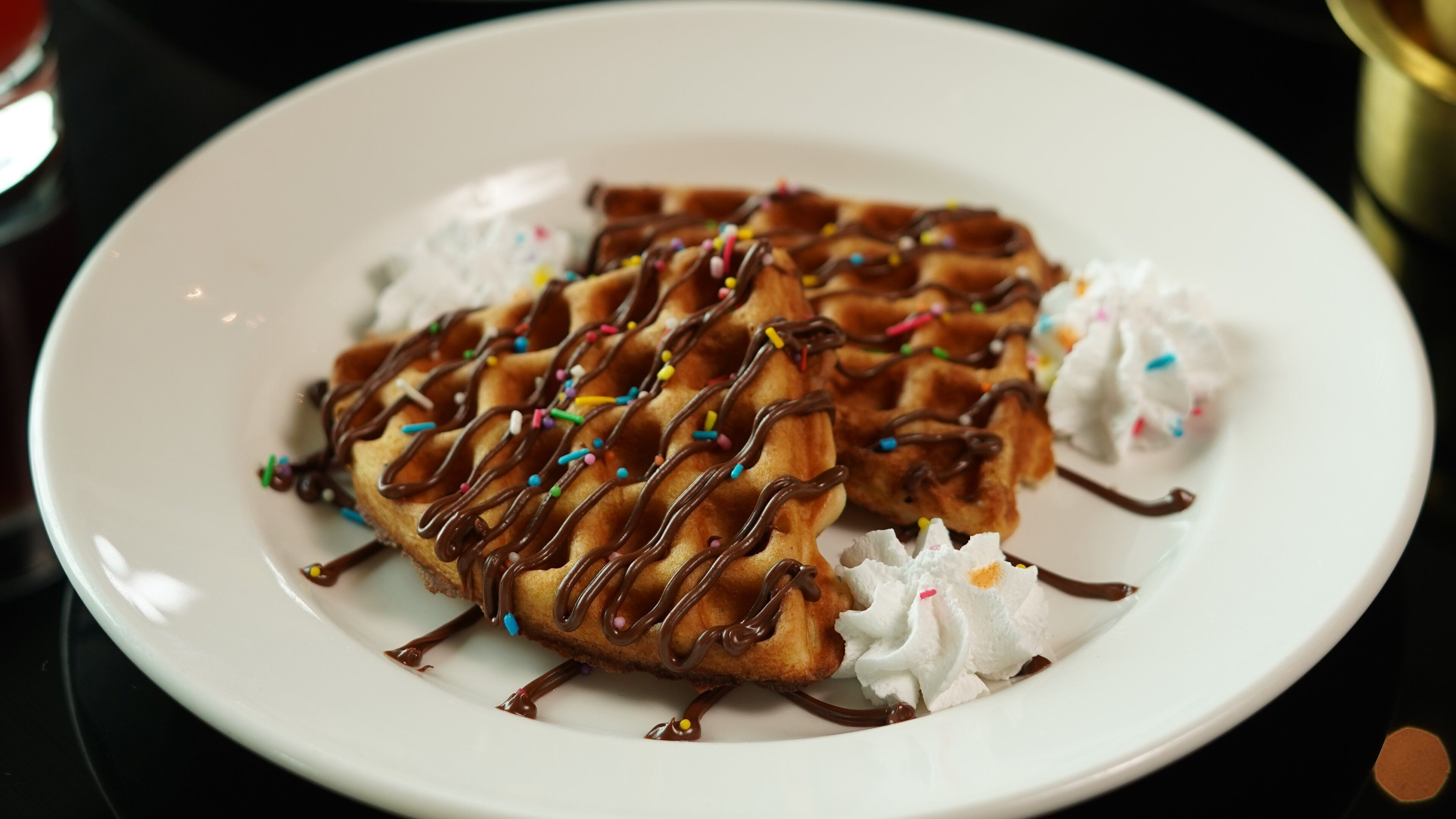 Un plato de waffles con goteado de chocolate y grageas de colores, acompañado de crema batida.