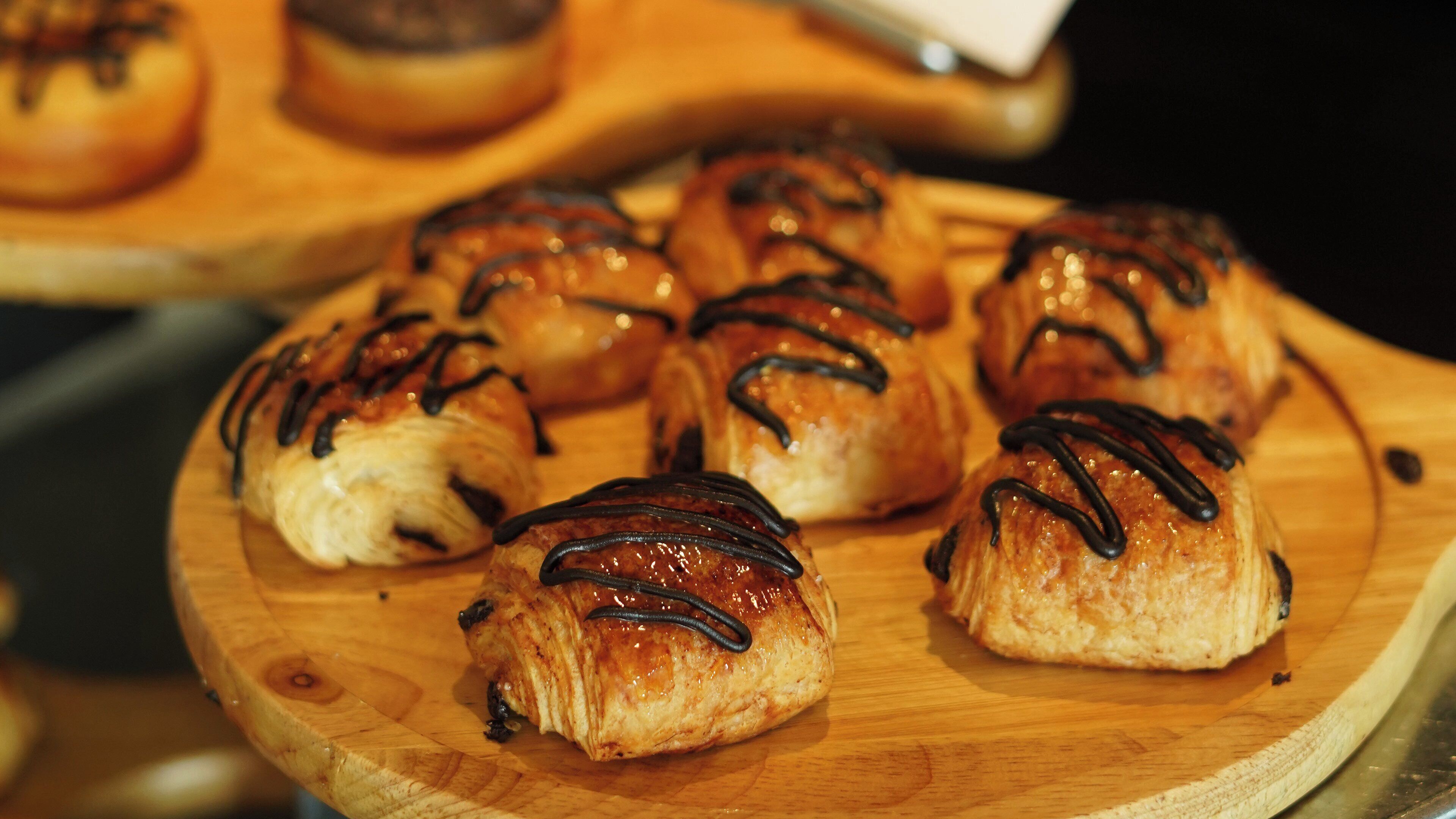 A wooden board with several pastries, each topped with a drizzle of chocolate.