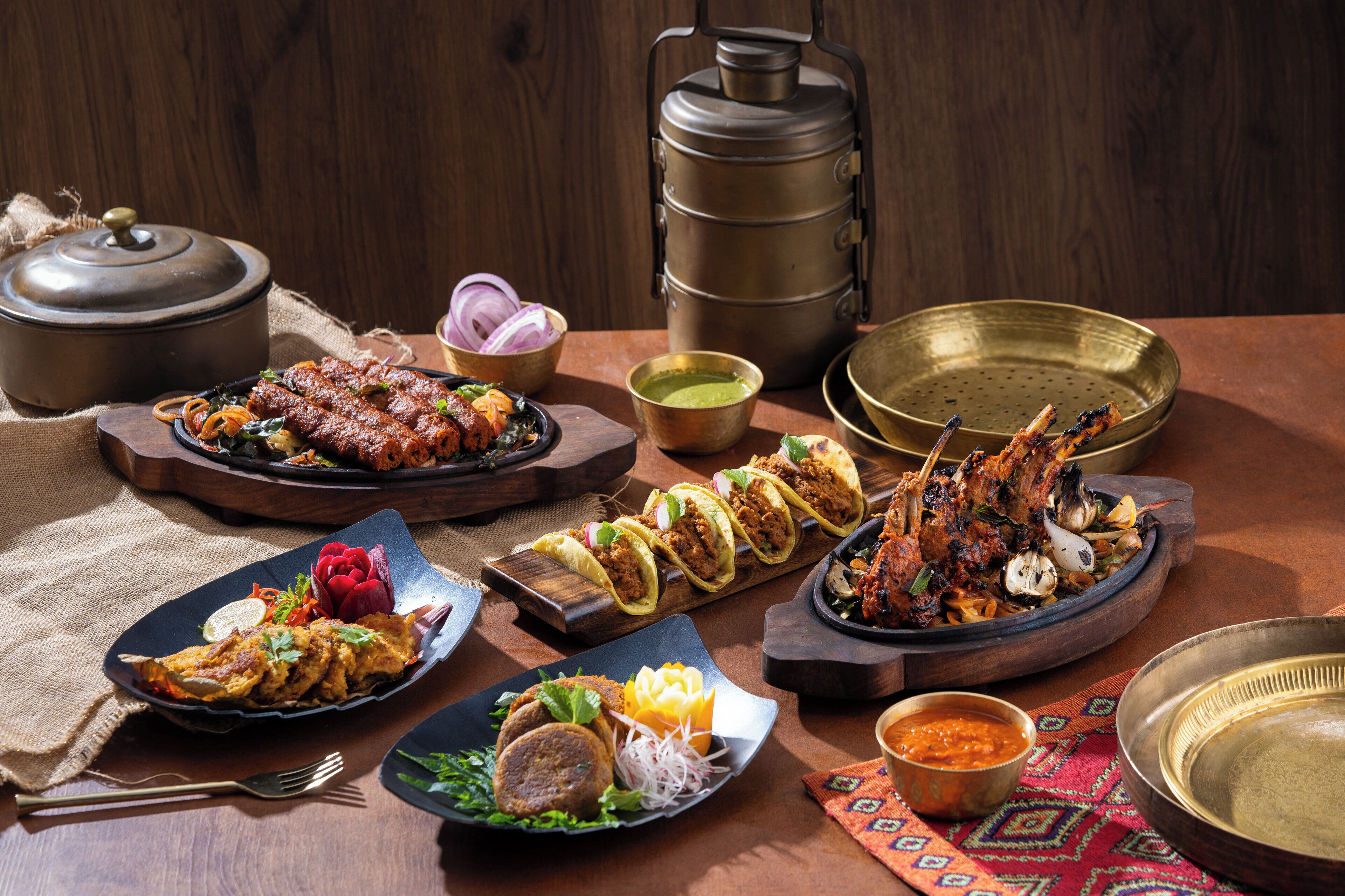 A variety of dishes on a wooden table, including tacos, grilled meat, and a large pot.