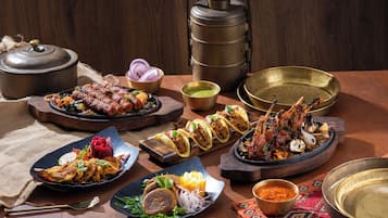 Une variété de plats sont disposés sur une table en bois, notamment des tacos, de la viande grillée et un grand plat.
