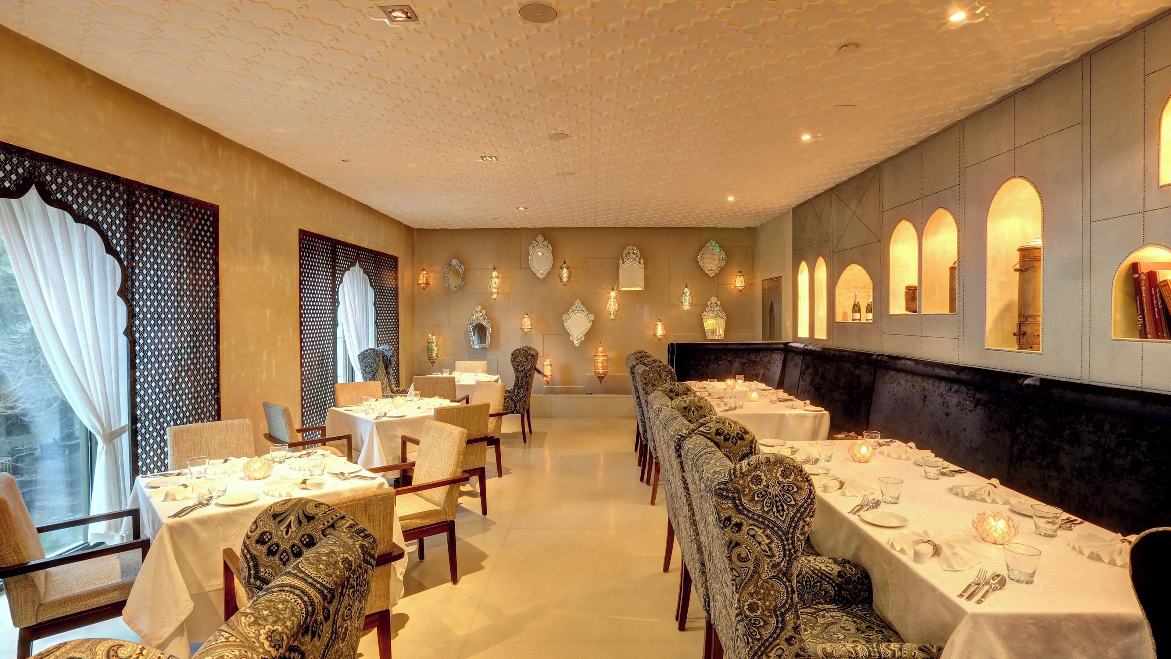 A dining area with tables set for service, patterned chairs, and decorative wall sconces.