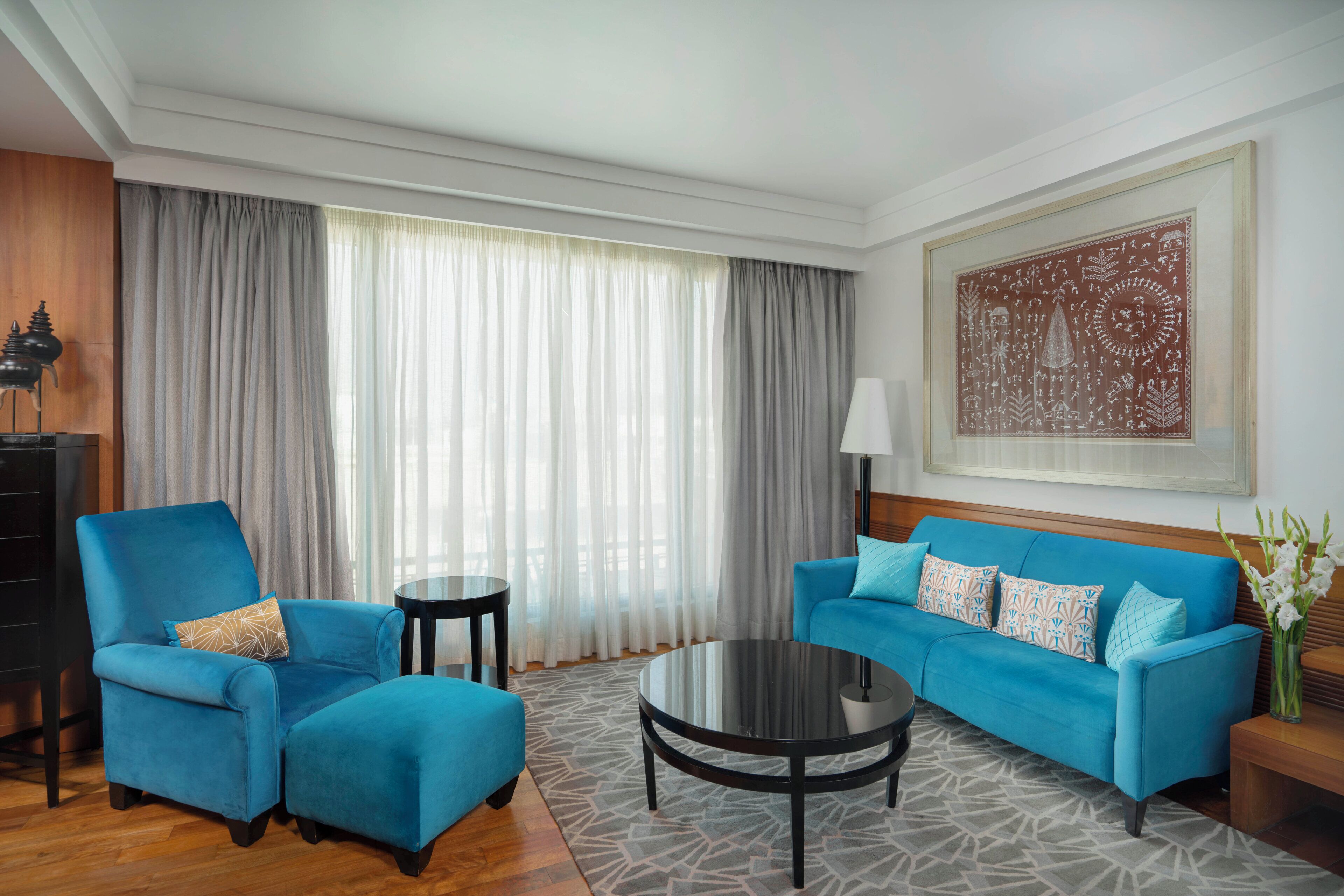 A hotel room with a blue sofa, a matching armchair, a small round table, and a large window with curtains.