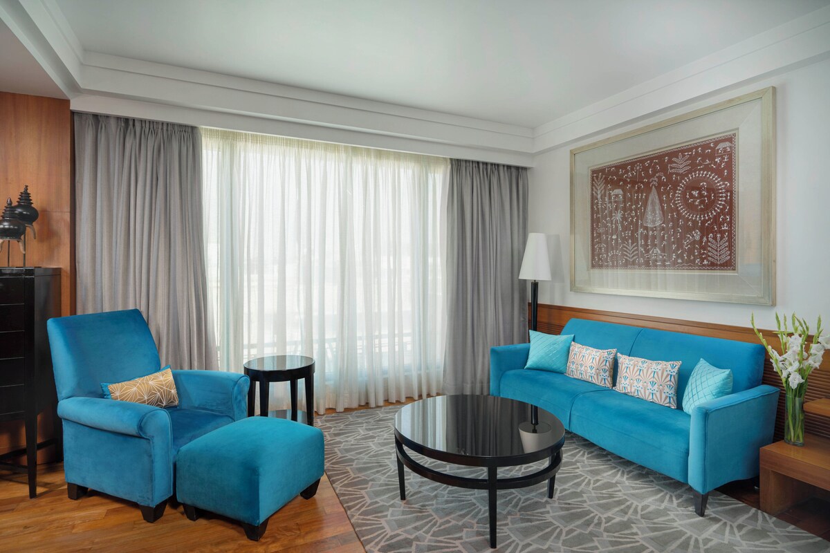A modern living room with a blue sofa, a matching armchair, a round coffee table, and a large window with sheer curtains.