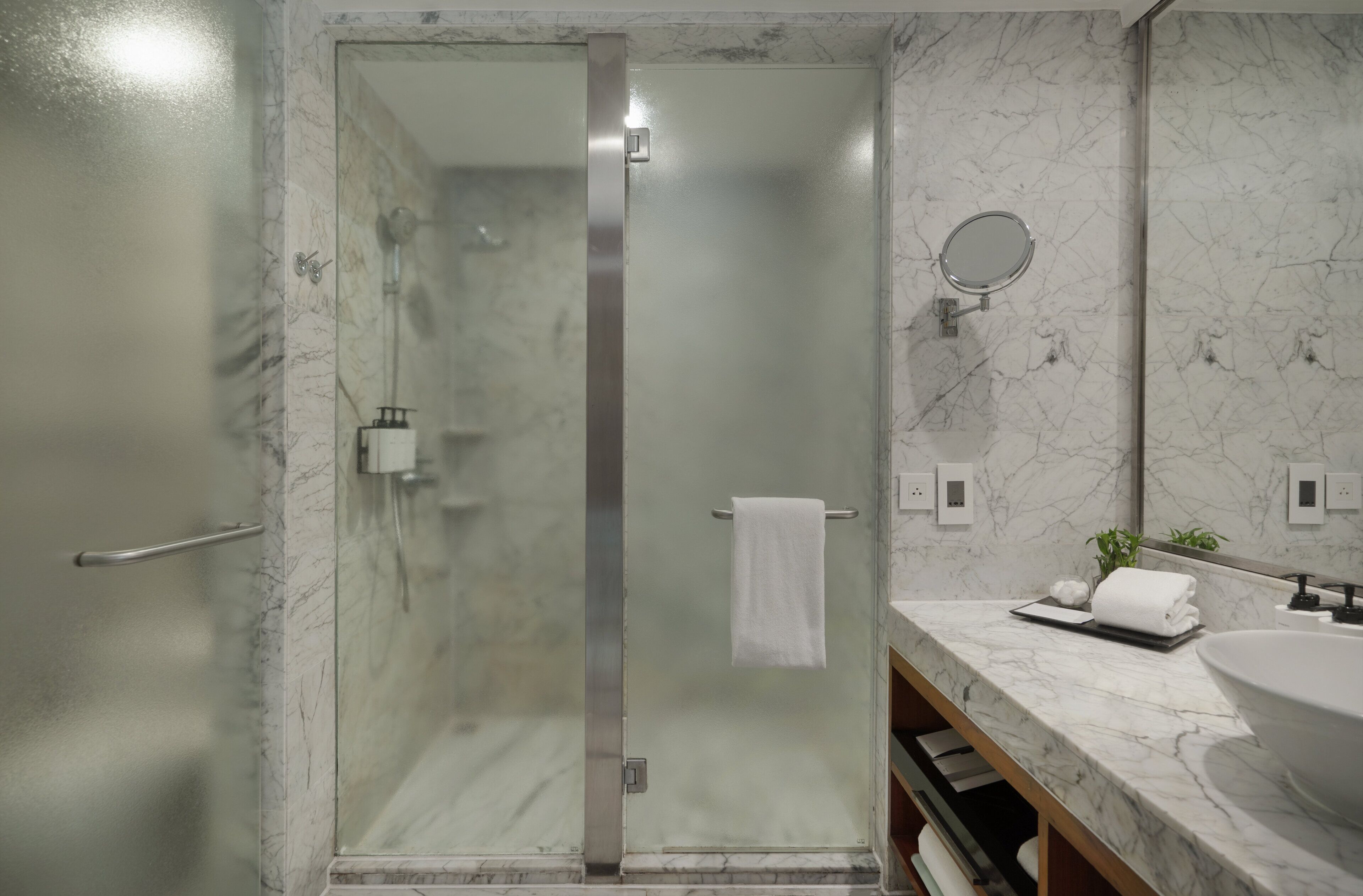 A modern bathroom with a glass-enclosed shower, a marble sink, and a mirror.