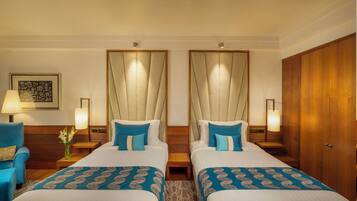 A hotel room with two beds, a wooden wardrobe, a nightstand with a lamp, and a framed picture on the wall.