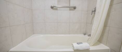 Una bañera blanca con un asidero, una toalla y una cortina de ducha en un baño con azulejos.