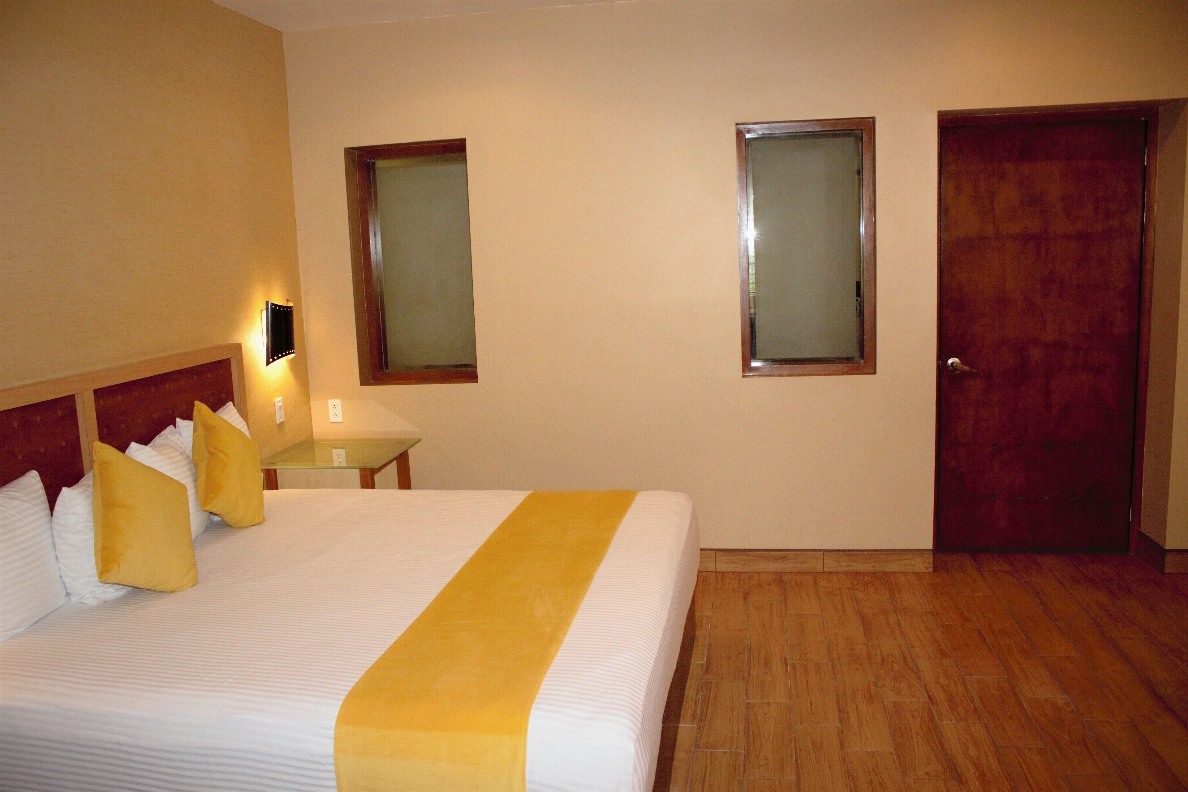 Una habitación de hotel con cama, mesita de noche, lámpara y puerta.