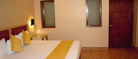 Una habitación de hotel con cama, mesita de noche, lámpara y puerta.