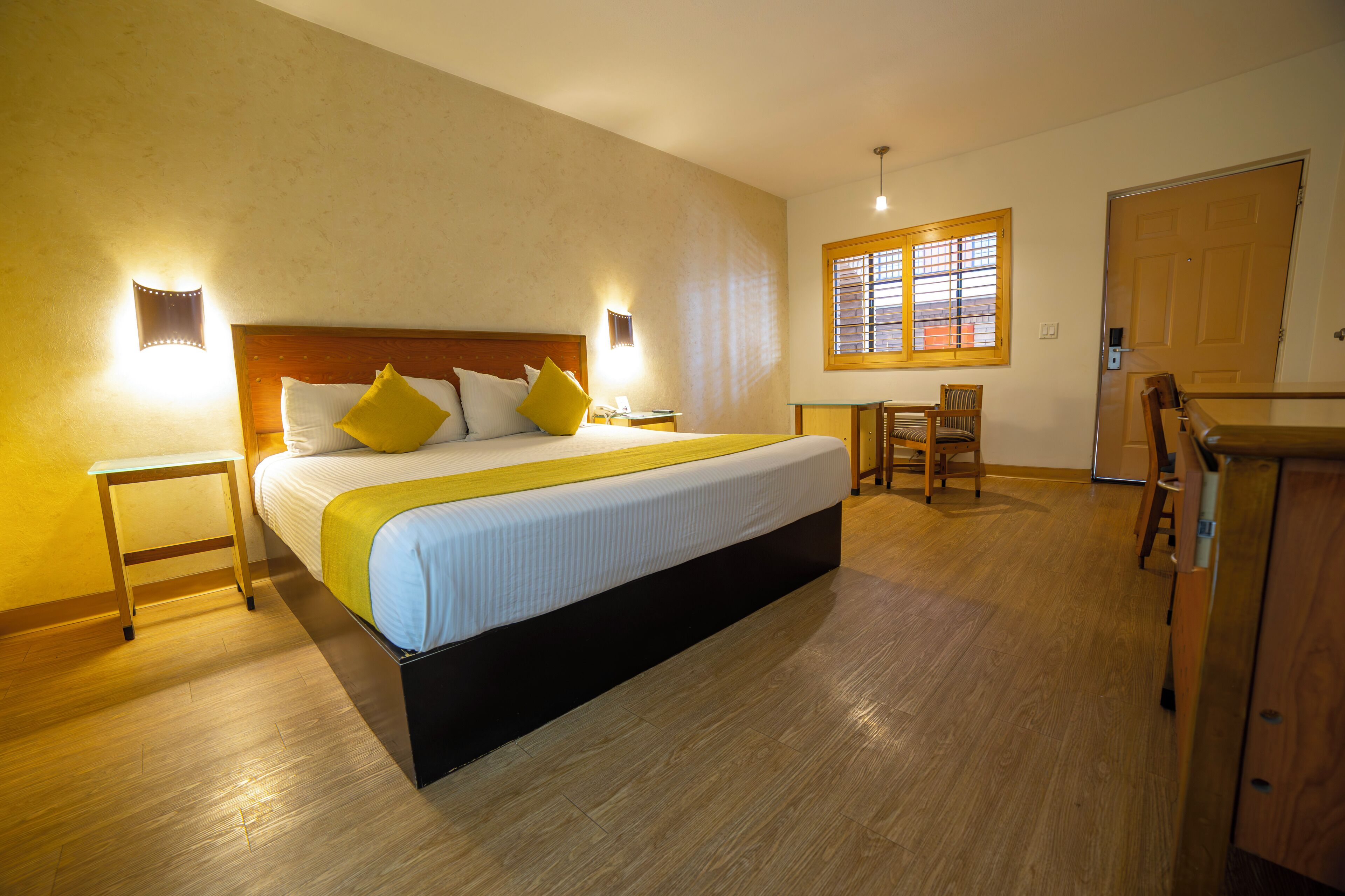 Ein Hotelzimmer mit einem großen Bett, einem Schreibtisch, einem Sessel und einem Fenster mit Jalousien.