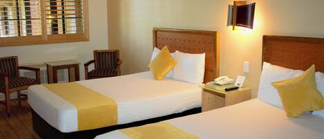 Een hotelkamer met twee bedden, een bureau, stoelen en een raam met zonwering.