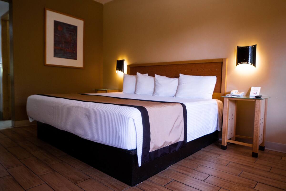 Un cuarto de hotel con una cama grande, una mesita de noche, una lámpara de pared y un cuadro enmarcado en la pared.