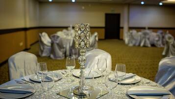 Una mesa de banquete dispuesta con manteles blancos, centros de mesa de cristal y cubertería.