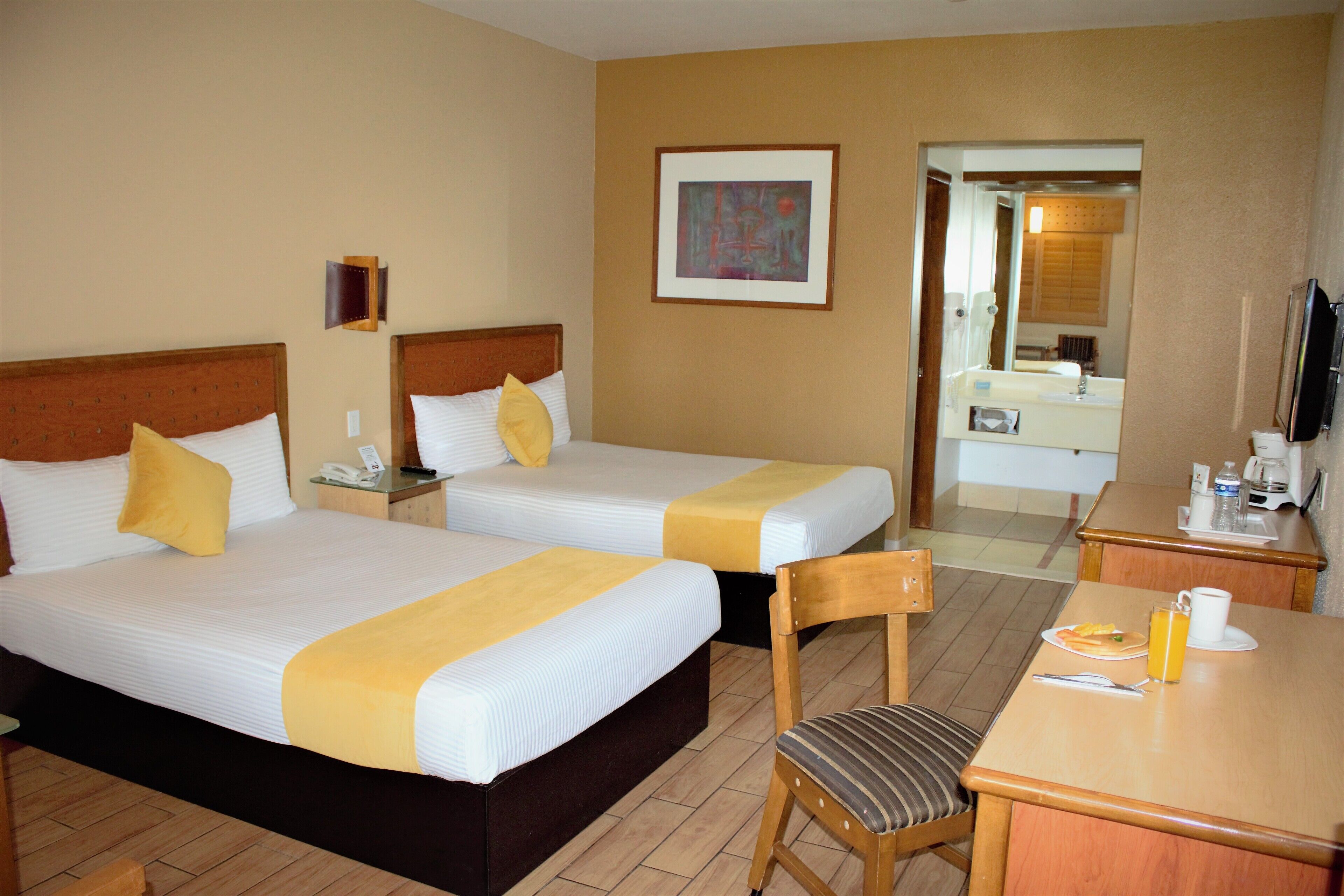 A hotel room with two beds, a desk, a chair, a mirror, and a television.