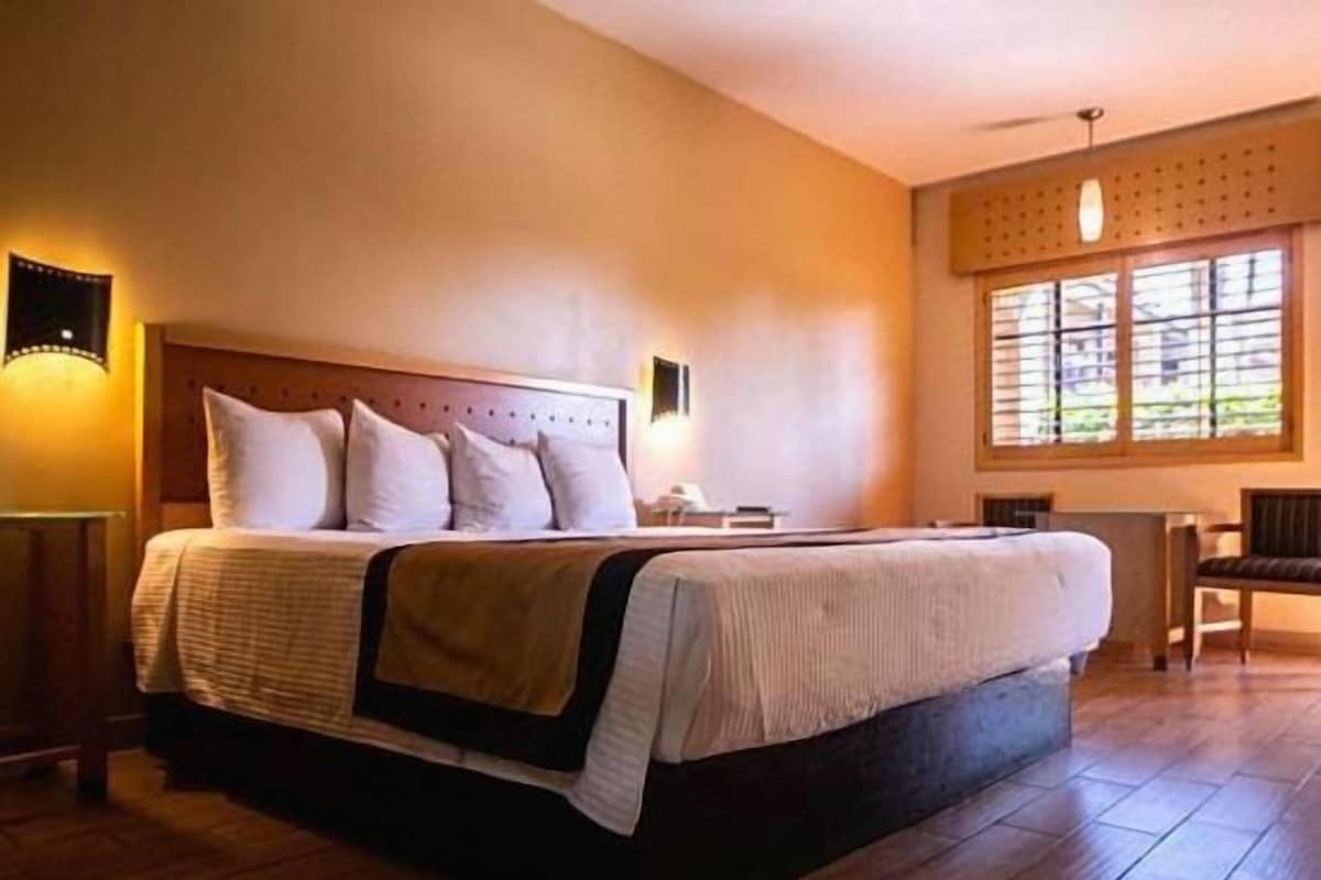 A bedroom with a large bed, a bedside table, a chair, and a window with blinds.