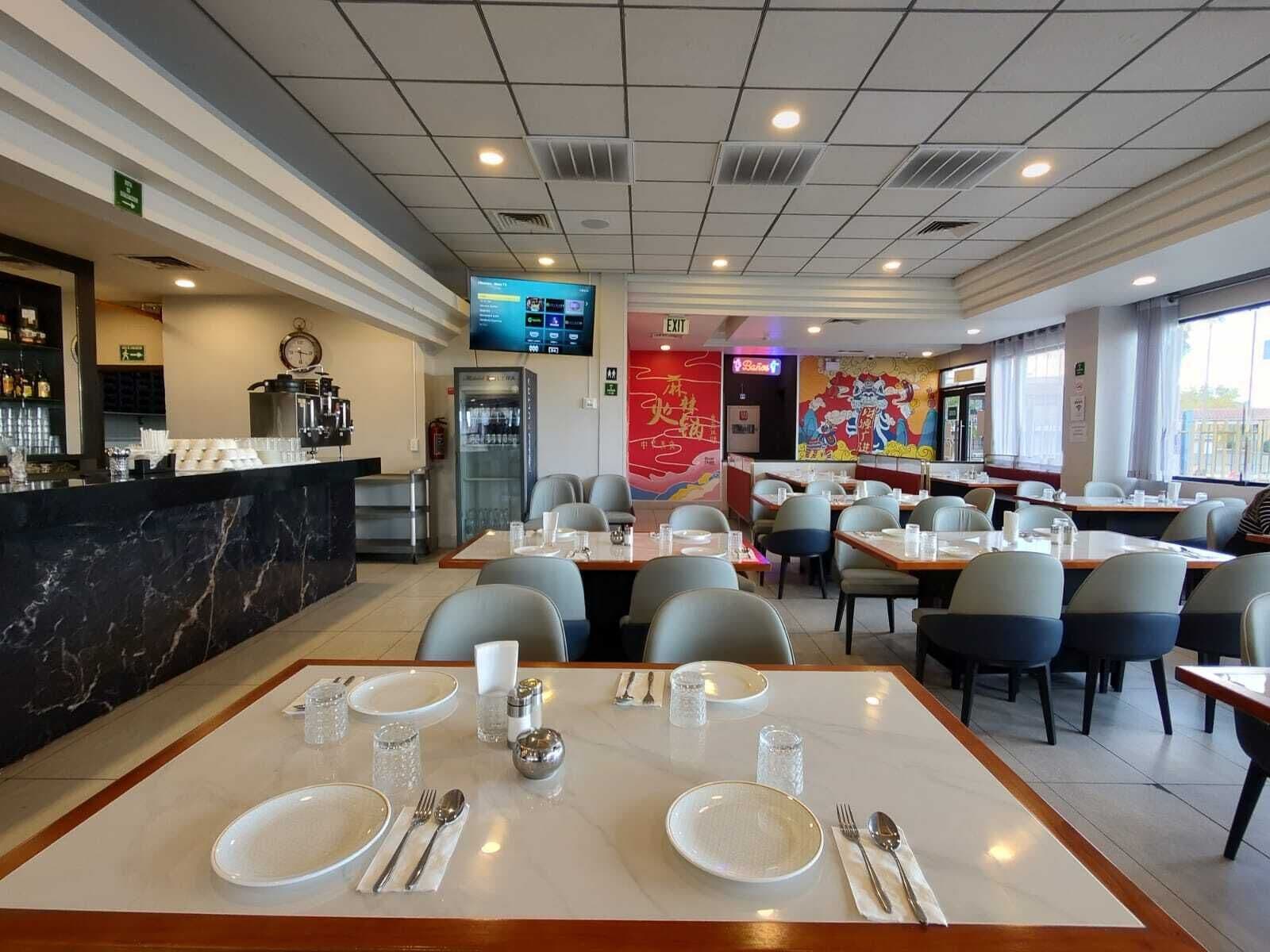 Un restaurant doté d’un comptoir en marbre, de tables dressées avec des assiettes, des couverts et des verres, et d’une fresque colorée sur le mur.