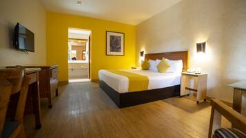 A hotel room with a bed, bedside table, lamp, and a desk with a chair.
