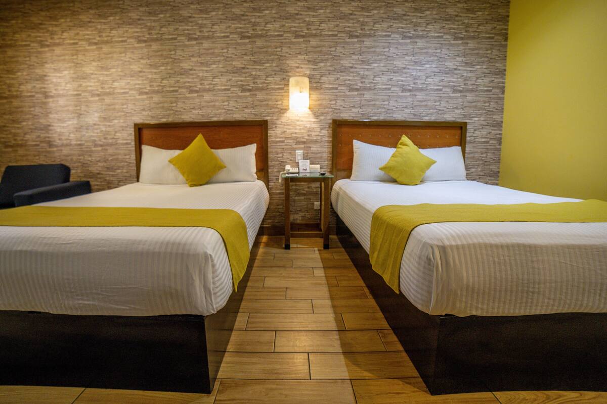 Una habitación de hotel con dos camas, una mesita de noche y una lámpara fijada a la pared.
