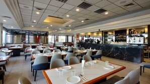 A spacious restaurant with multiple tables and chairs, a bar area with a marble countertop, and a view of the outside through large windows. - Hotel Colonial Mexicali (Mexicali)