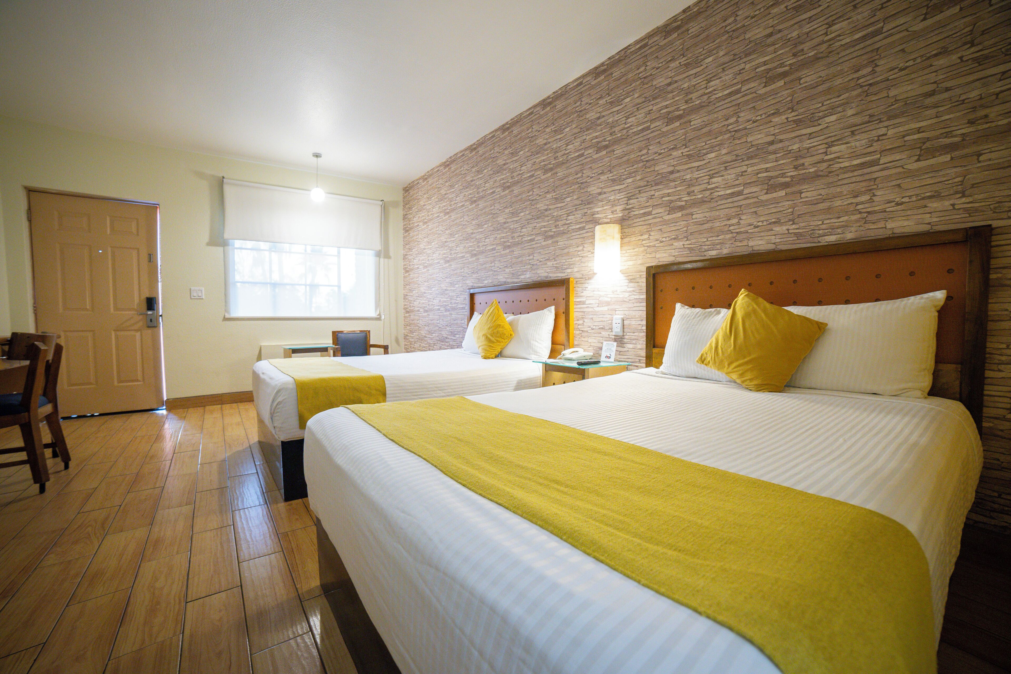 Une chambre d’hôtel avec deux lits, un plancher en bois, un mur décoratif en briques et une fenêtre avec des stores.