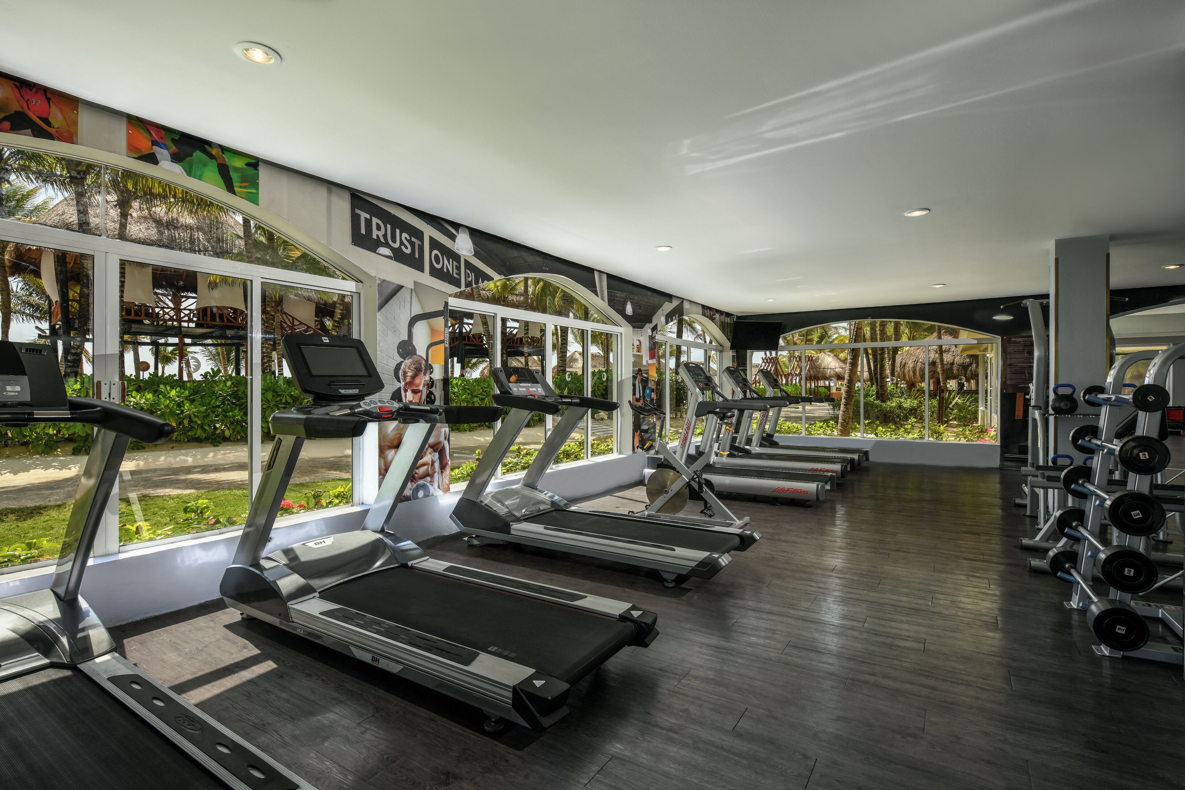 A gym with treadmills, weight machines, and a large window with a view of greenery.