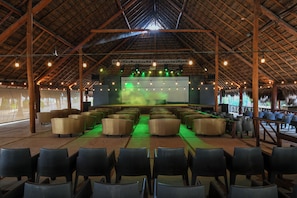 An indoor venue with a stage, seating, and a thatched roof structure.