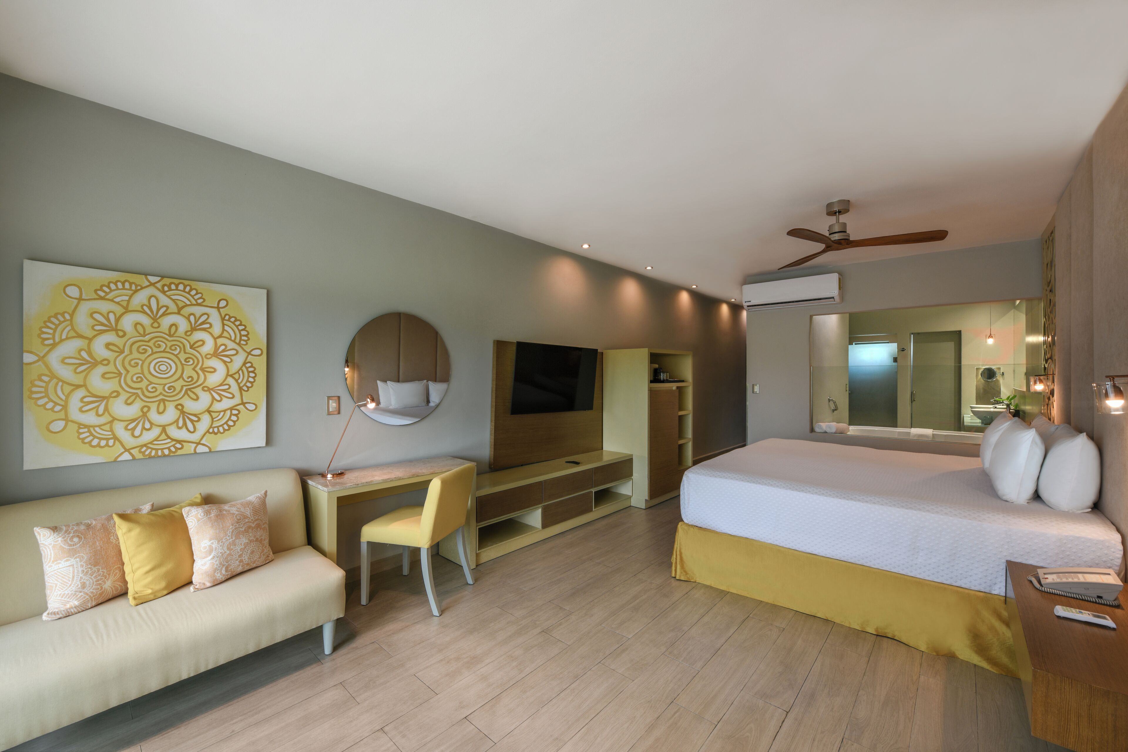 A modern hotel room with a bed, a desk, a sofa, a TV, and a ceiling fan.