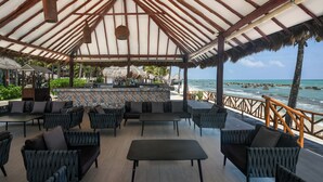 A covered outdoor seating area with a bar, wicker furniture, and a view of the ocean. - El Dorado Royale, All & More Inclusive Adults Only (Playa del Carmen)