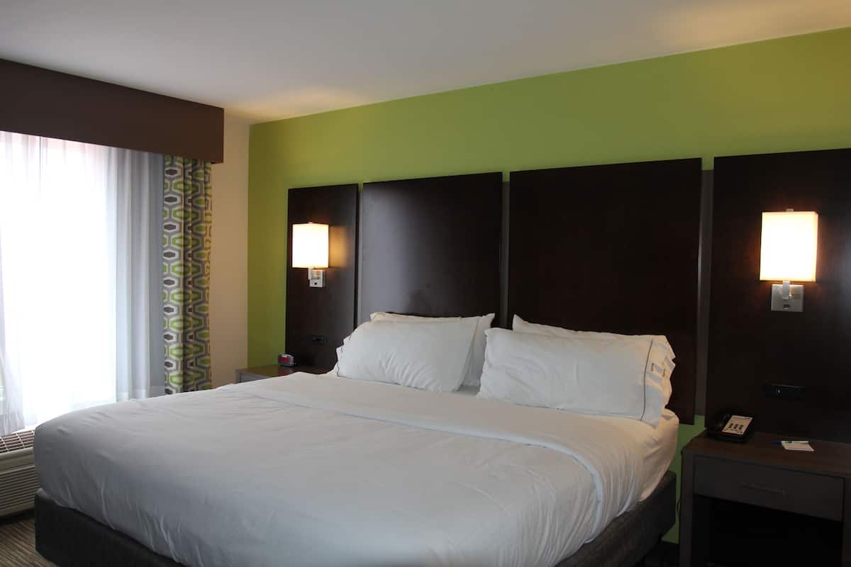 Una habitación de hotel con una cama grande, dos lámparas de noche, una mesita de noche con un teléfono y una ventana con cortinas.