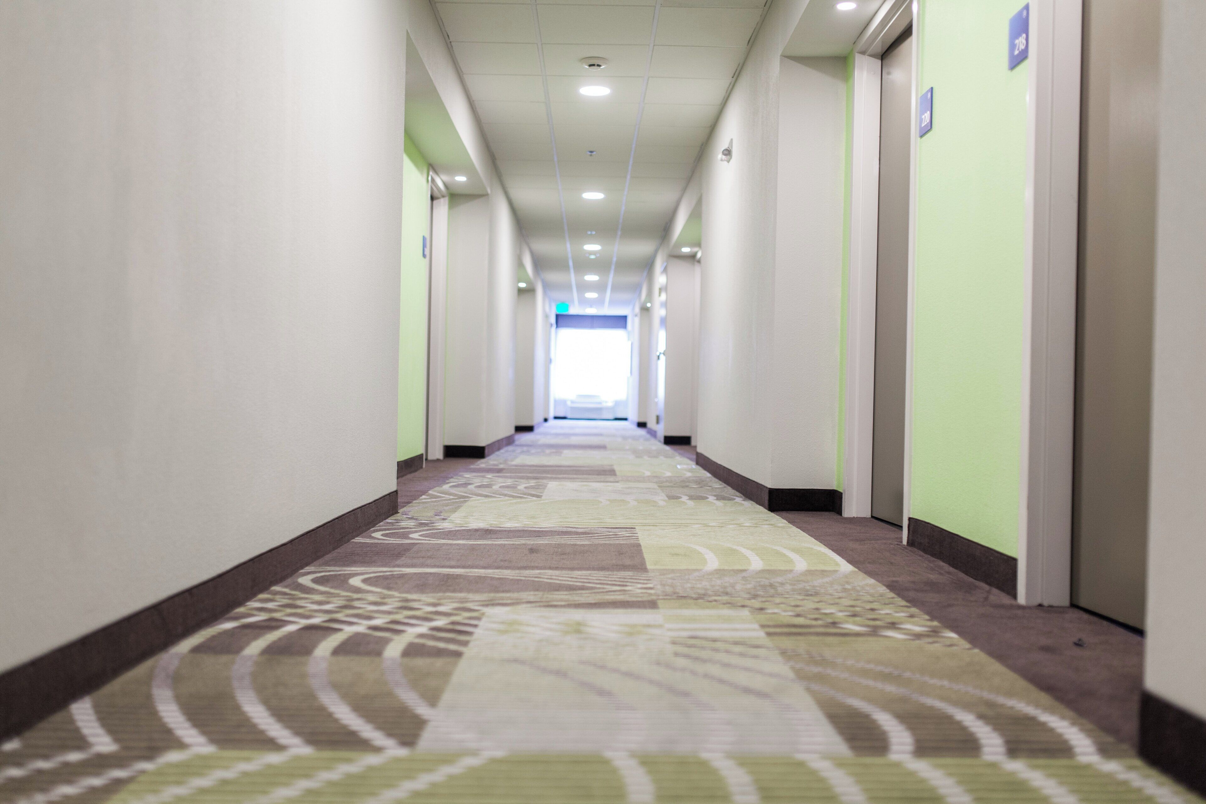 Un pasillo largo y estrecho en un hotel, con pisos alfombrados y puertas a ambos lados que dan a habitaciones individuales.