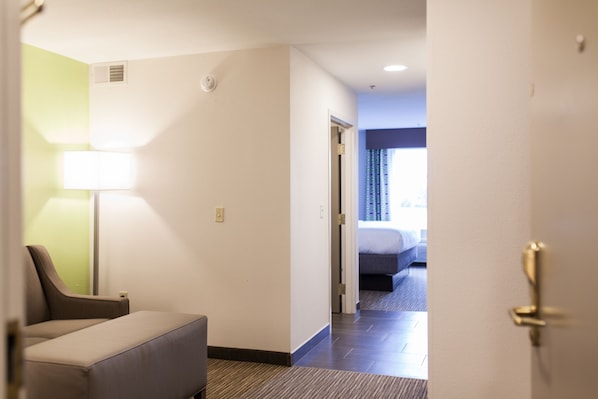 Une chambre d’hôtel avec un lit, un bureau et une chaise. Une porte donne accès à une autre pièce.
