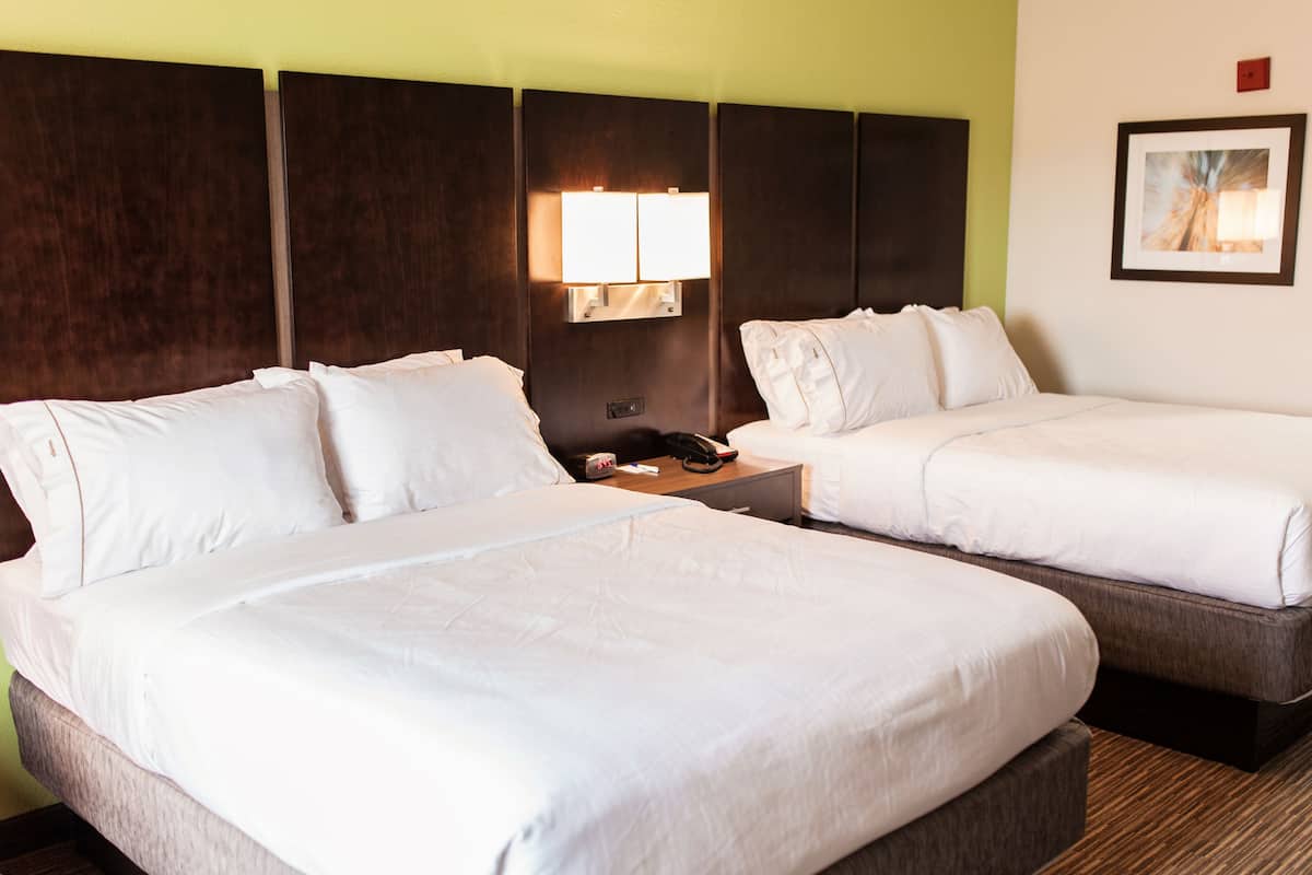 Habitación de hotel con dos camas, una mesita de noche con teléfono y una lámpara de pared.