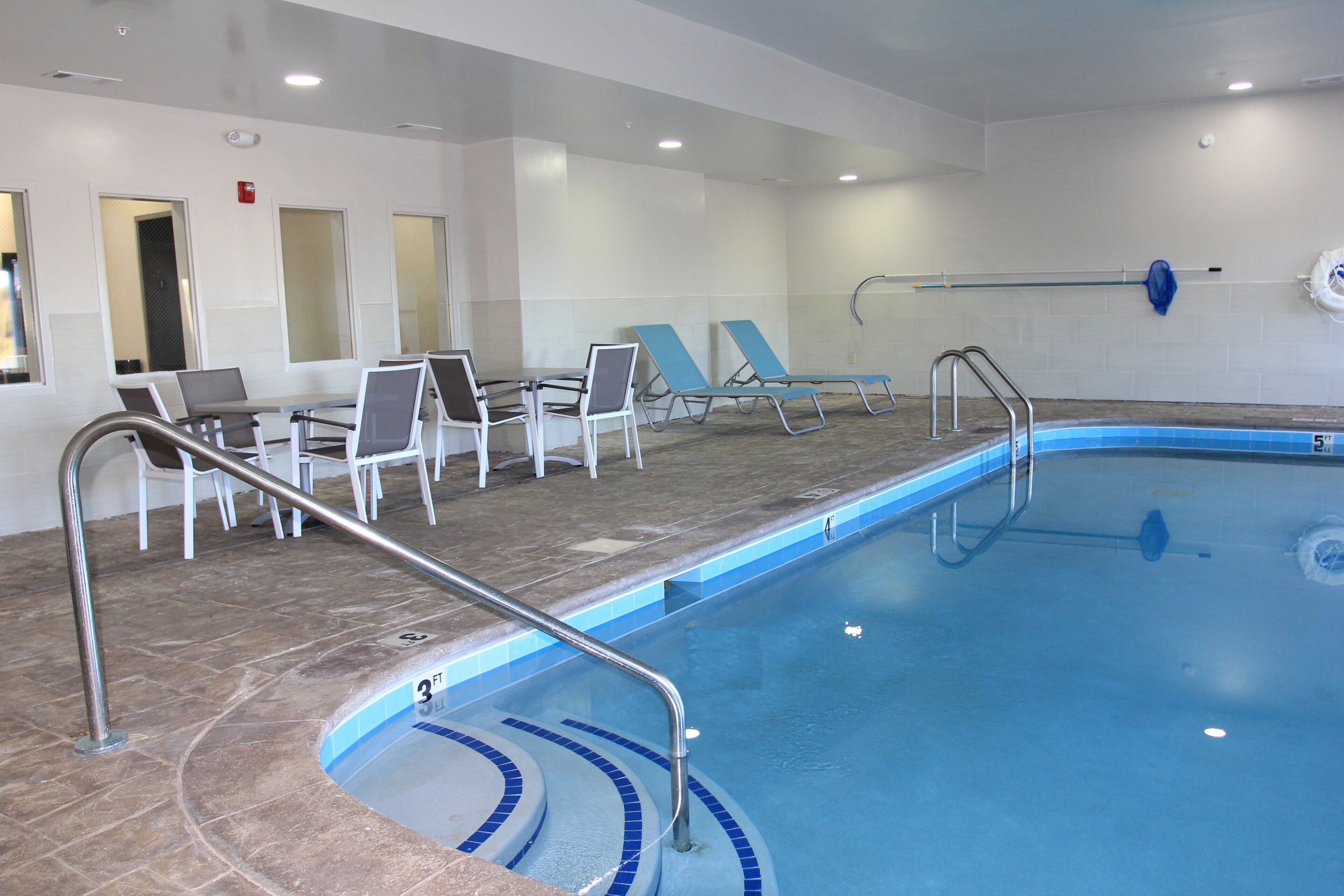 An indoor swimming pool with a 3ft and 5ft depth marking, surrounded by lounge chairs and a table with chairs.