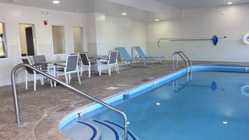 An indoor swimming pool with a 3ft and 5ft depth marking, surrounded by lounge chairs and a table with chairs.