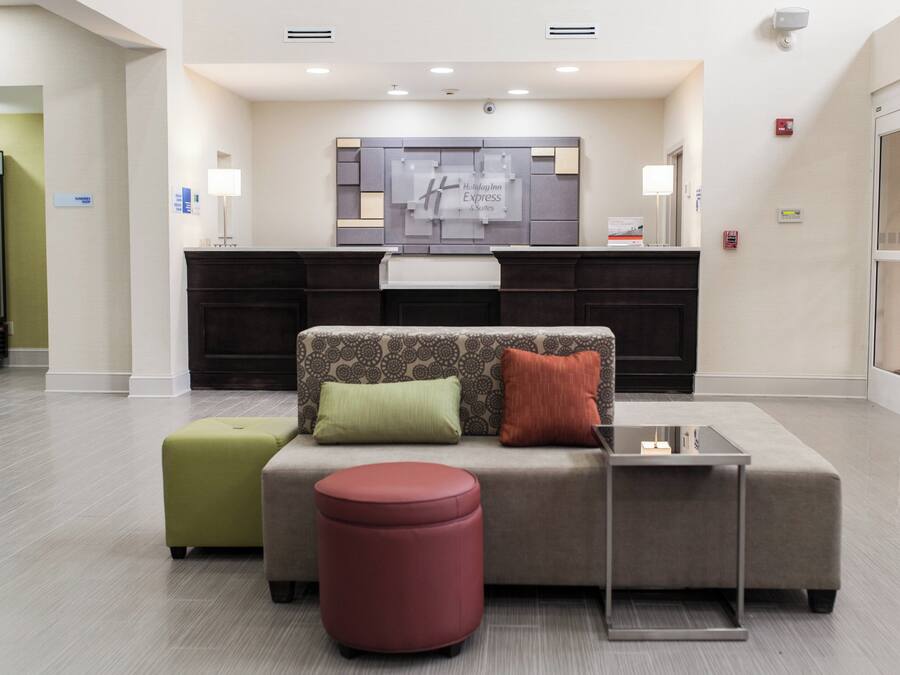 A modern hotel lobby with a reception desk, a sofa with cushions, a small ottoman, and a glass coffee table.
