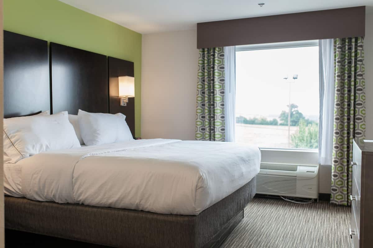 Una habitación de hotel con una cama grande, una ventana con cortinas, un aire acondicionado de pared y una mesita de noche.