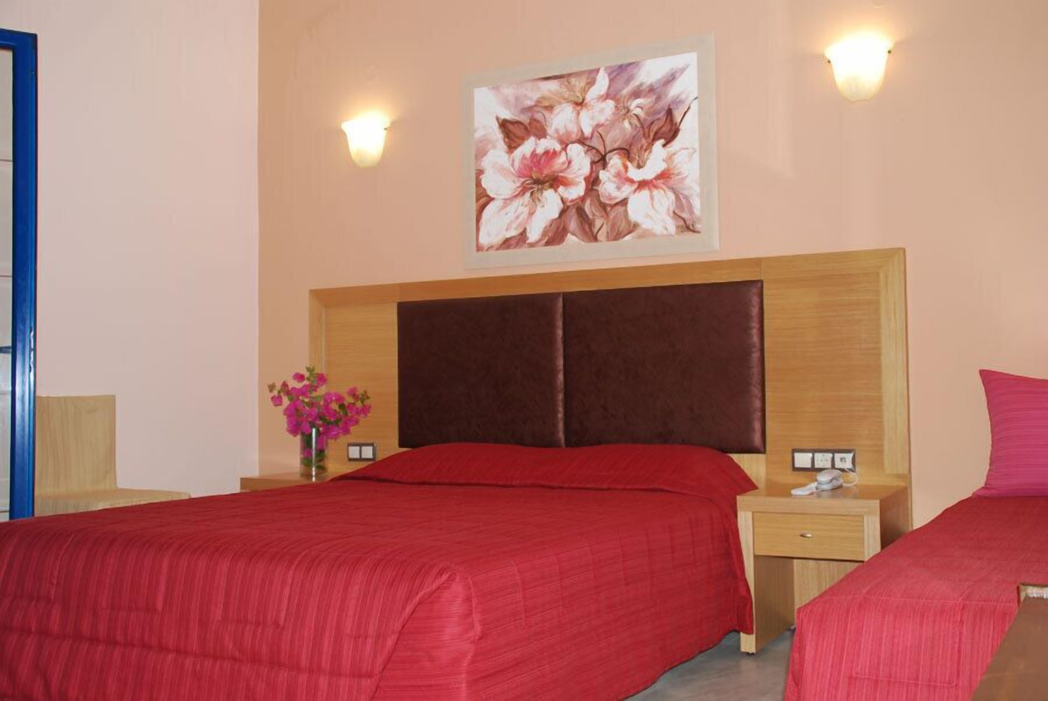 A hotel room with two beds, a wooden headboard, a floral painting, and a vase with flowers.