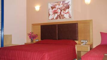 A hotel room with two beds, a wooden headboard, a floral painting, and a vase with flowers.