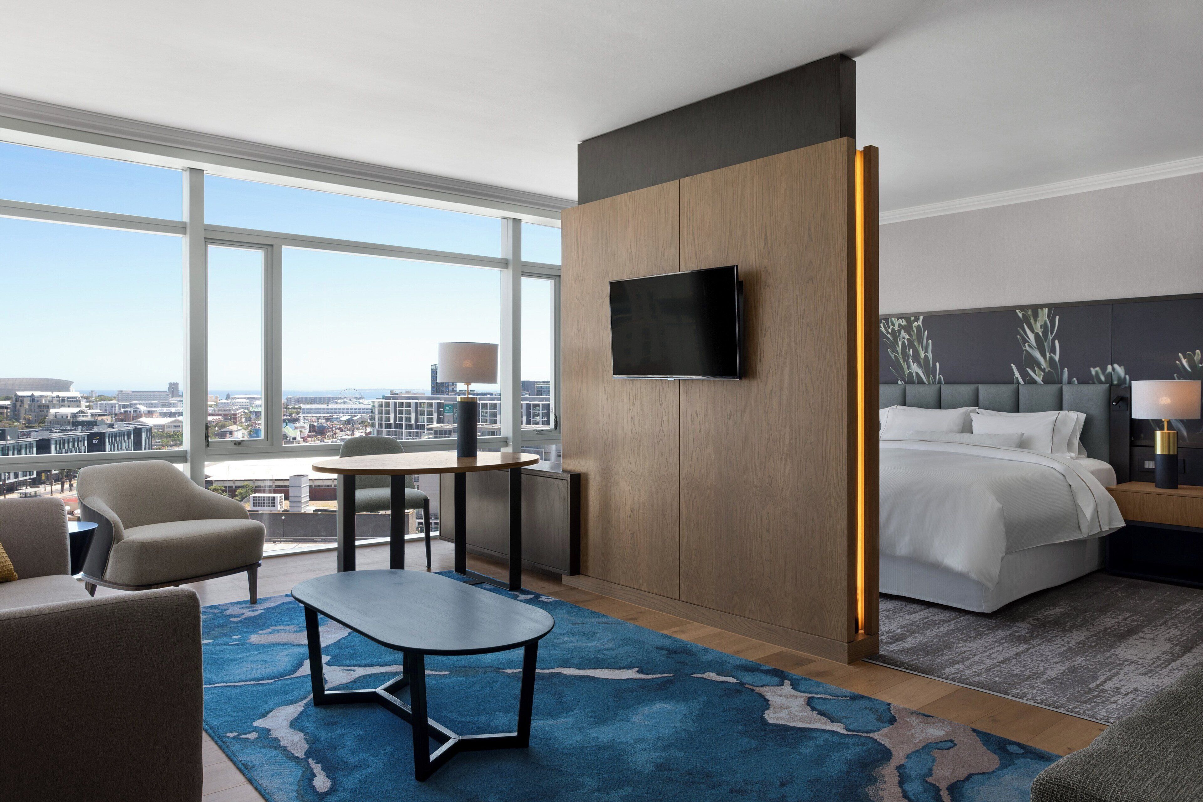 Ett hotellrum med ett stort fönster, en säng, en tv, ett skrivbord och en stol.