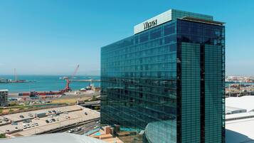 Un hotel Westin moderno con fachada de vidrio, situado cerca de un puerto con grúas visibles y un estacionamiento.