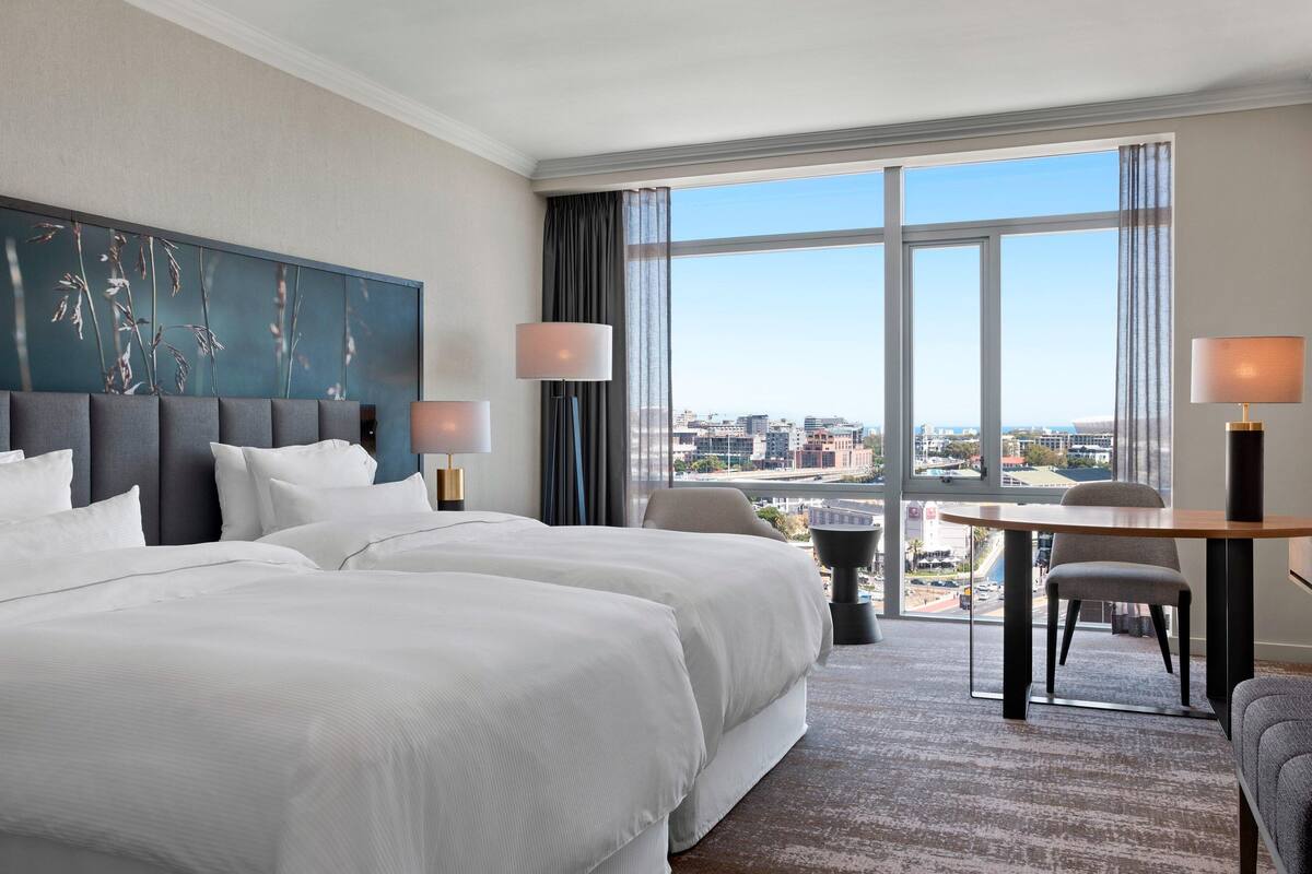 Een hotelkamer met twee bedden, een eettafel en uitzicht op de stad.