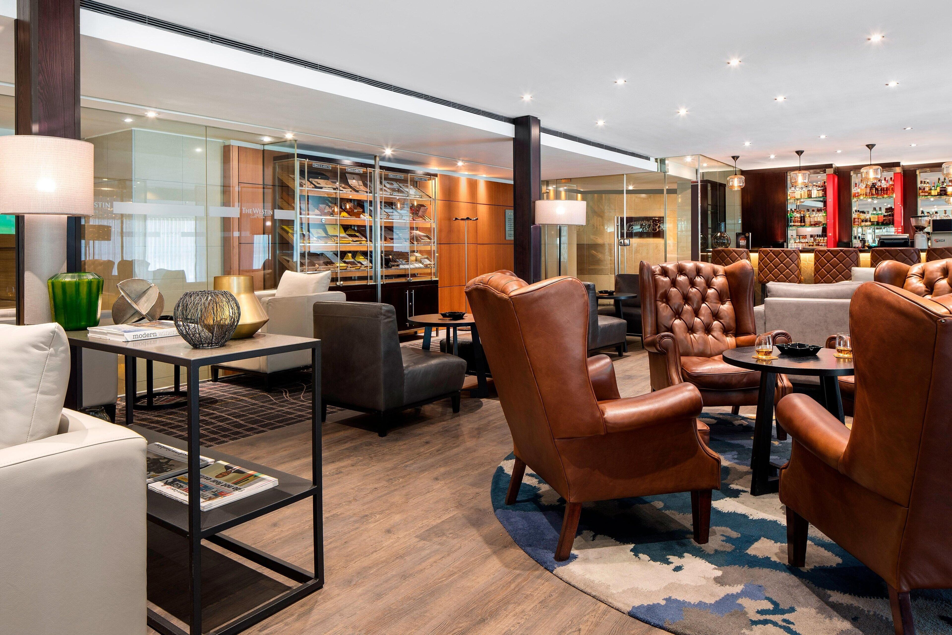 A modern lobby with leather armchairs, a glass shoe display, and a bar area.