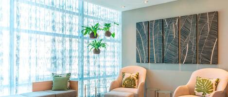Una sala de estar moderna con un sofá, dos sillones, una mesa de centro y un ventanal con plantas.