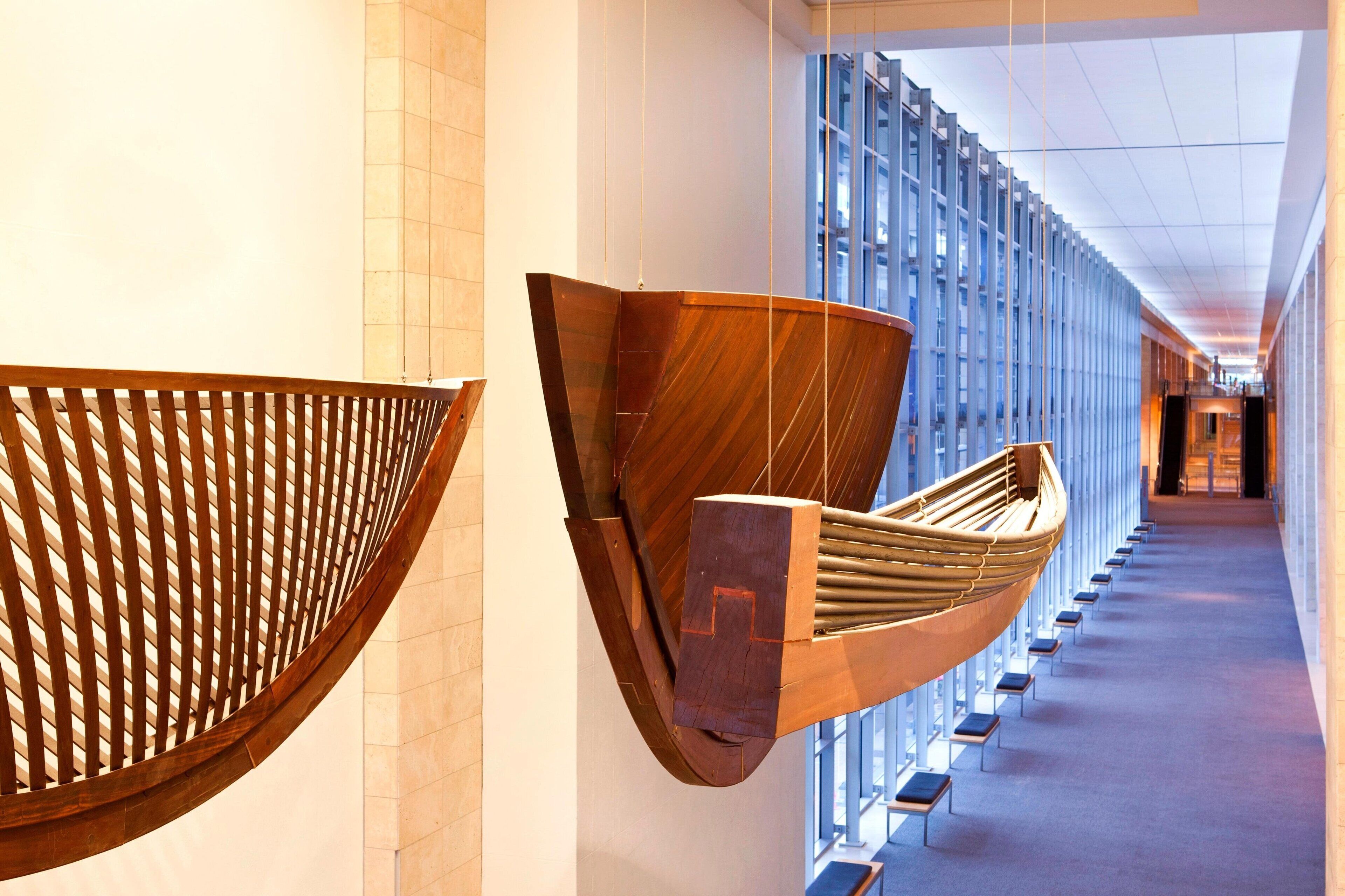 A corridor with modern wooden art installations and a view of a building through large windows.