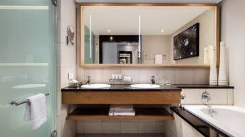 A modern bathroom with two sinks, a large mirror, and a bathtub.